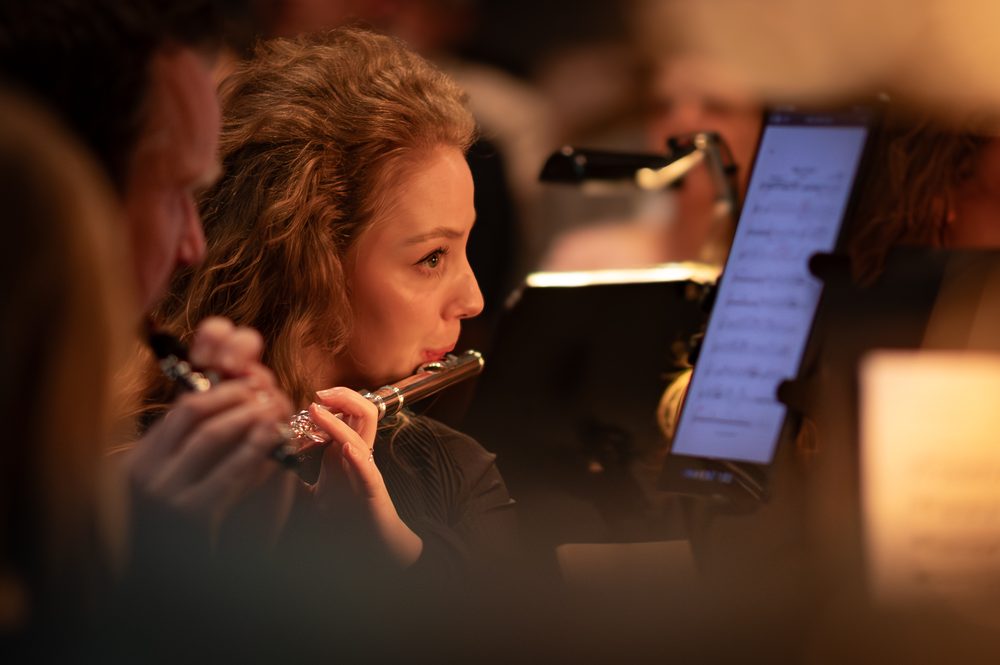 Fluitiste in een orkest, gezien door een warme onscherpe voorgrond, naast een muziekstandaard met bladmuziek