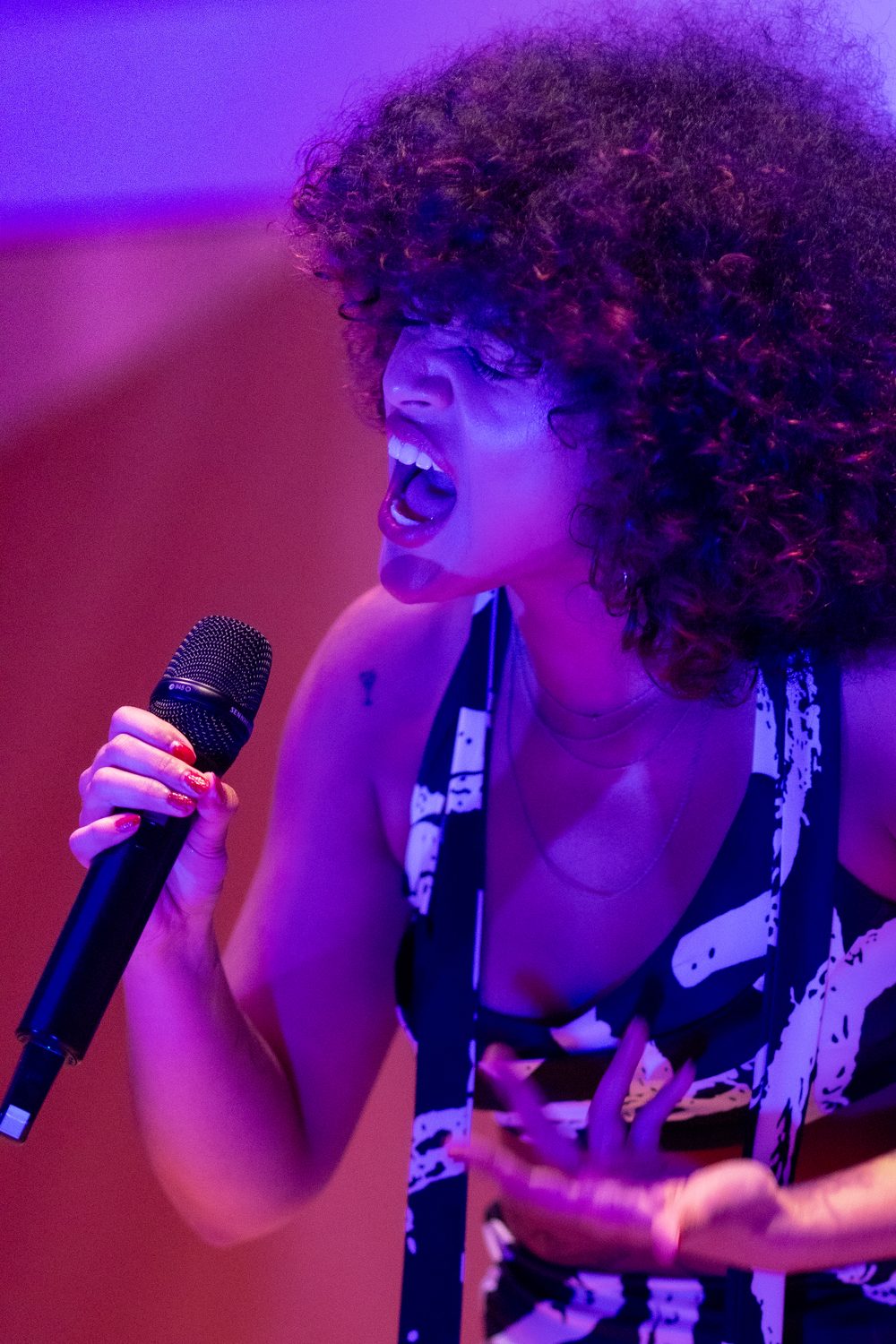 Zangeres met een grote bos krullen zingt met volle inzet in paars en rood podiumlicht